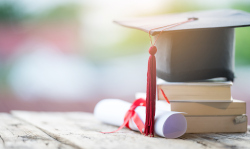 A graduation cap on top of a stack of books on a park bench