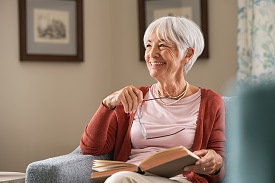 An elderly woman holding a book and glasses