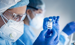 Researcher wearing a mask examining a vial of vaccine