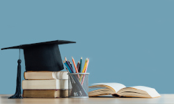 A graduation cap laying on a stack of books, next to a cup full of pencils and an open book, untop a table