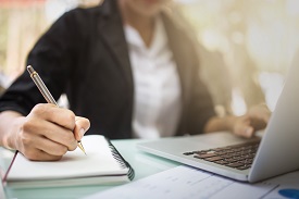 a person using a laptop and writing in a notebook