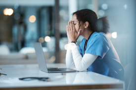 Frustrated nurse sitting at a desk with her hands on her face