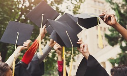 Students in graduation regalia hold up their graduation caps