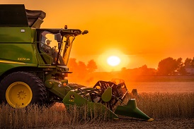 the sun sets behind a tractor in a soybean farm