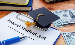 A graduation cap and small piles of money next to a note pad with the words Federal Student Aid