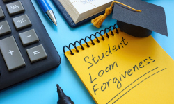 A desk with a keyboard, a book, a pen, and a note pad with the words Student Loan Forgiveness