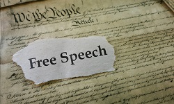 A torn piece of paper saying free speech sits atop a replica of the constitution