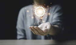A woman holds up an icon of a glowing bulb with a gear inside it; the glowing bulb symbolizes innvoation and creativity