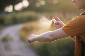 A person spraying bug spray on their arm