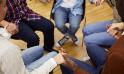 Individuals sitting in a circle holding hands