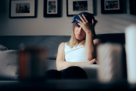 A woman sitting on a couch holding an ice pack to her head