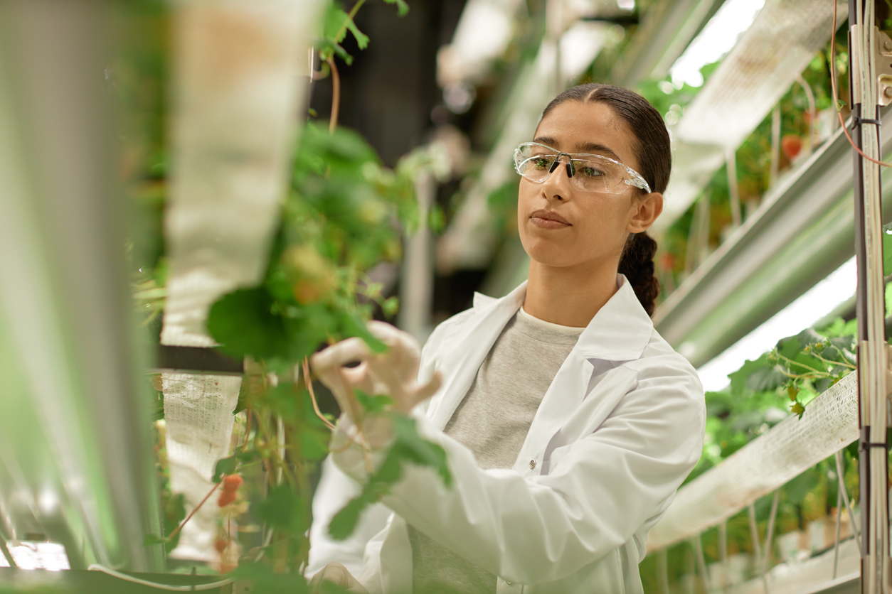 Researcher in a lab coat with plants. 