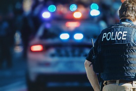 A police officer faces a police vehicle with its lights on