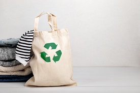 A cloth bag with the recycling symbol sits next to a stack of clothes