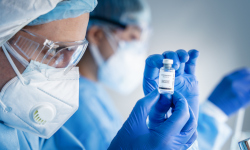researcher in scrubs and a facemask looking at a vial.