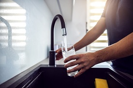 A person fills a glass under a running faucet