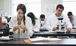 Students wearing lab coats using microscopes in a classroom