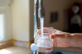 An open faucet pouring water into glass