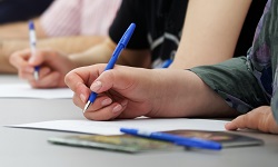 People writing something on paper in a workshop-like setting. Only their hands are visible.