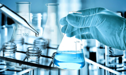 a gloved hand holding a beaker with liquid in it and a dropper next to it
