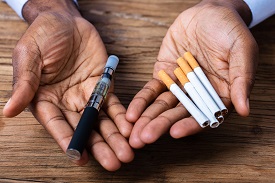 a person holds an e-cigarette in one hand and cigarettes in the other