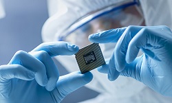 Design engineer in sterile coverall holds microchip with gloves and examines it

