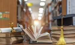 Stacks of books with a college diploma and graduation cap