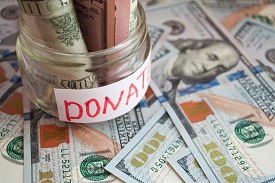 A jar of money labelled donate sits atop hundred dollar bills