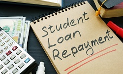 A notepad and a calculator. Student Loan Repayment is written on the notepad.