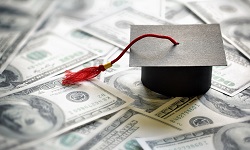 A small paper graduation hat sits atop money spread around
