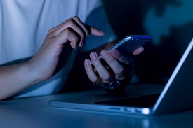 a person uses a phone in front of a laptop in a dark setting