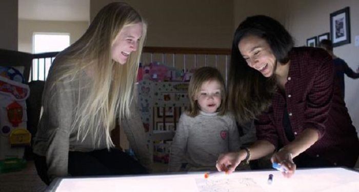 Undergraduate research associate Allie Coy (left) and CU Boulder instructor Lameese Akacem (right) play with a child over a light table.