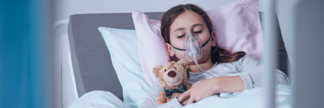 Sick young girl in a hospital bed sleeping with an oxygen mask and a toy, getting treatment for cystic fibrosis.