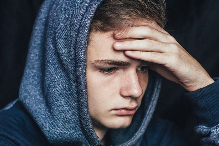 Image of teenage boy with hand on forehead.