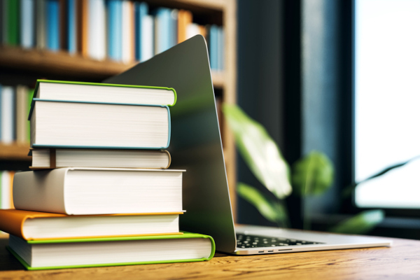 Stack of books next to an open laptop