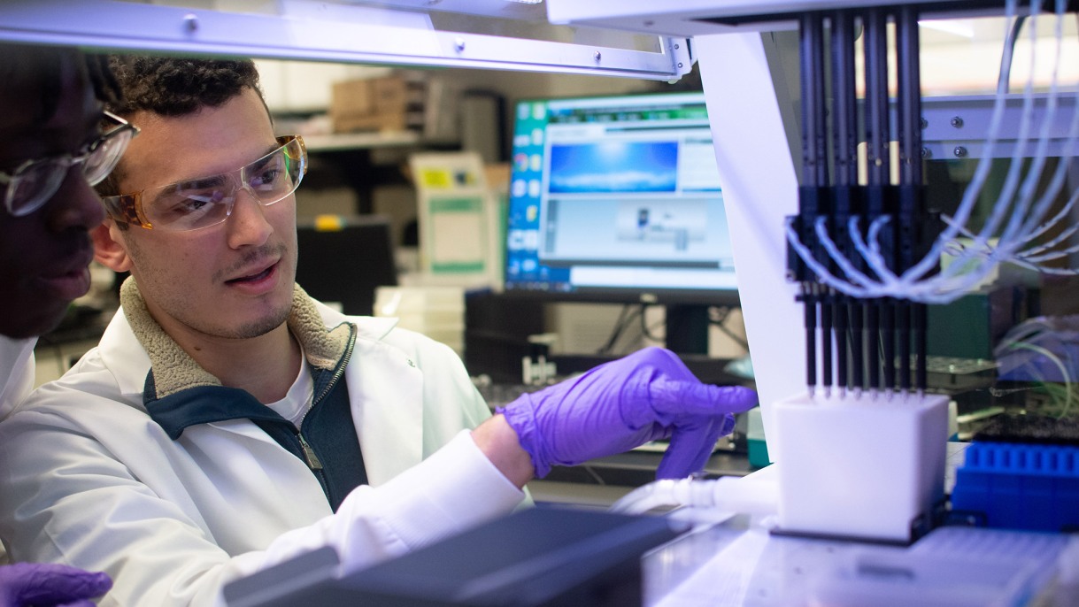 "Undergraduates David Okoh and Adam Spooner take a close look at the robotic liquid handler their research group used to make a powerful diagnostic tool simpler and more automated. All photos by Juan Siliezar/Brown University."