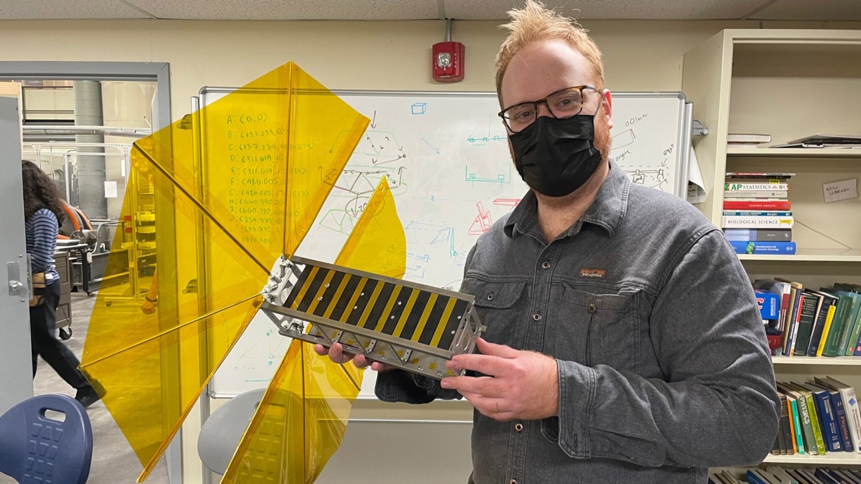 "Satellite built by Brown students and launched by SpaceX shows a low-cost way to reduce space debris; Marco Cross, who graduated from Brown last year with a master’s degree in biomedical engineering and served as the project's chief engineer, holding the SBUDNIC satellite. Image courtesy of Marco Cross."
