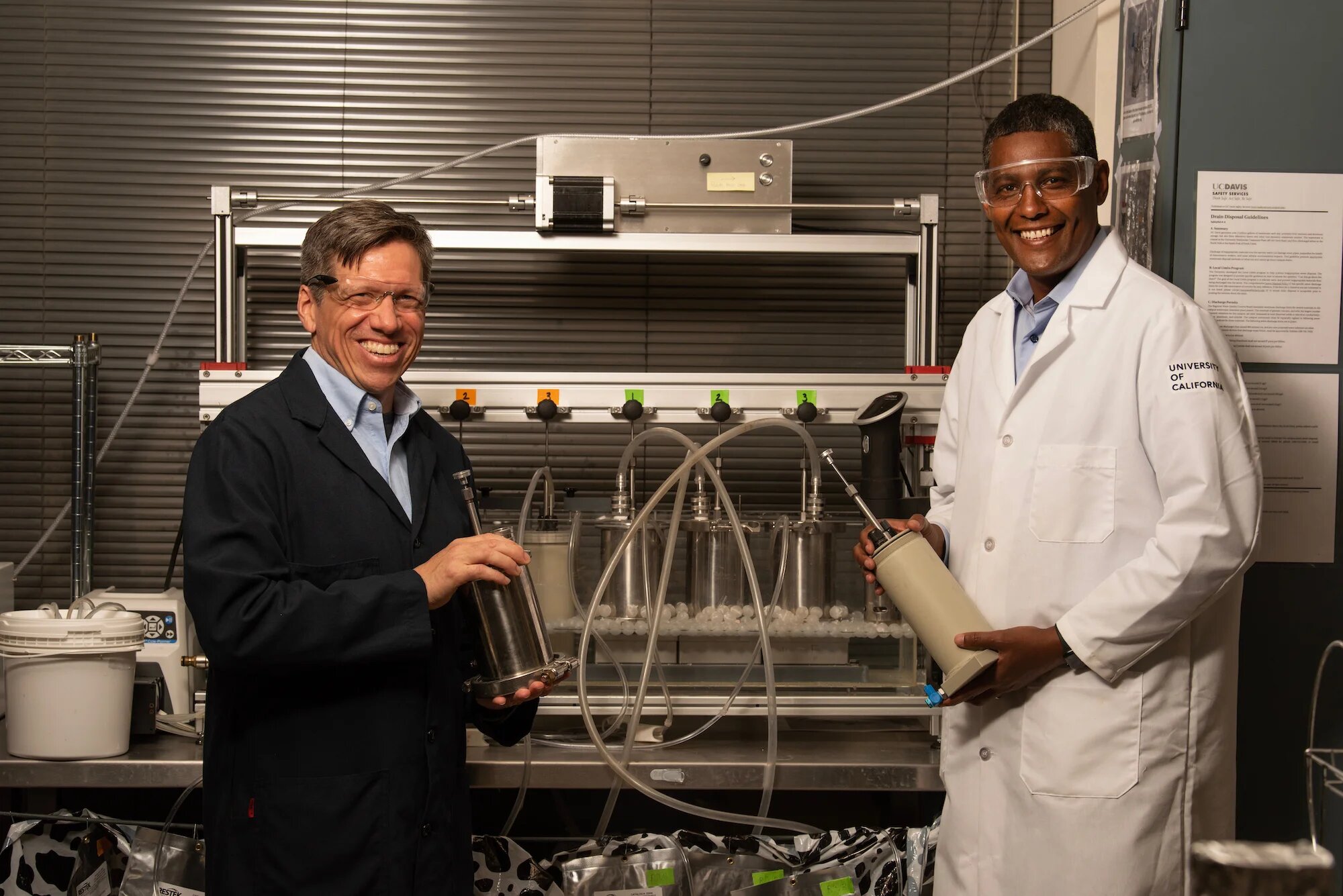 "Can CRISPR Cut Methane Emissions From Cow Guts?; Matthias Hess, left, and Ermias Kebreab, right, stand in front of a system that mimics a cow's rumen and allows Hess to study gas-producing microbes. (Gregory Urquiaga/UC Davis)"