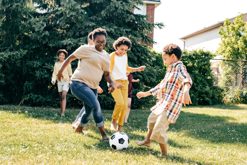 Physical spaces where kids live, play and learn have big impact on obesity, eating behaviors; Picture: children and teens playing soccer outside on grass.