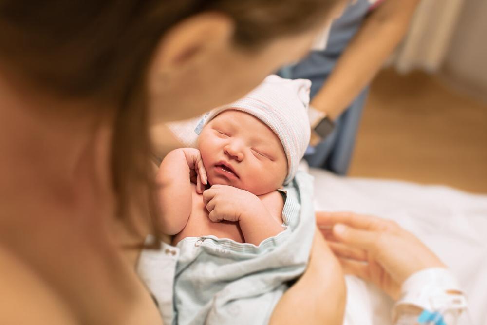 "Common Pregnancy Complications May Delay Development of Infant in the Womb; Stock image of newborn baby in mothers arm"
