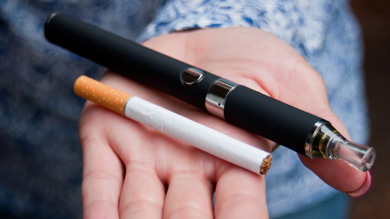 "DNA Damage Levels Similar in Vaping and Smoking, Study Finds; Photo of cigarette and vape in open hand, iStock"