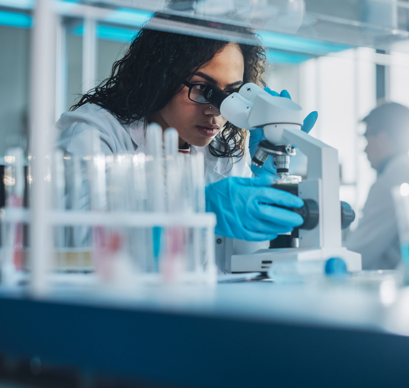 Researcher in a lab coat looking at a speciment with a microscope