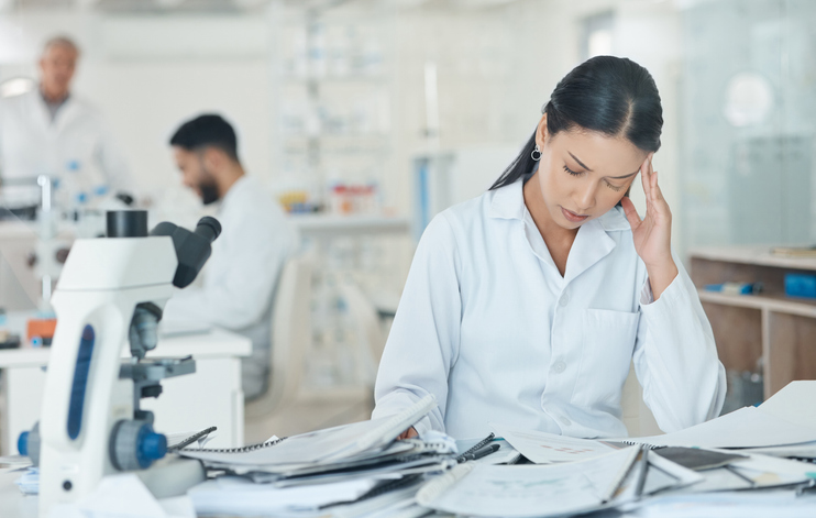 Scientist looks stressed behind a pile of paperwork.
