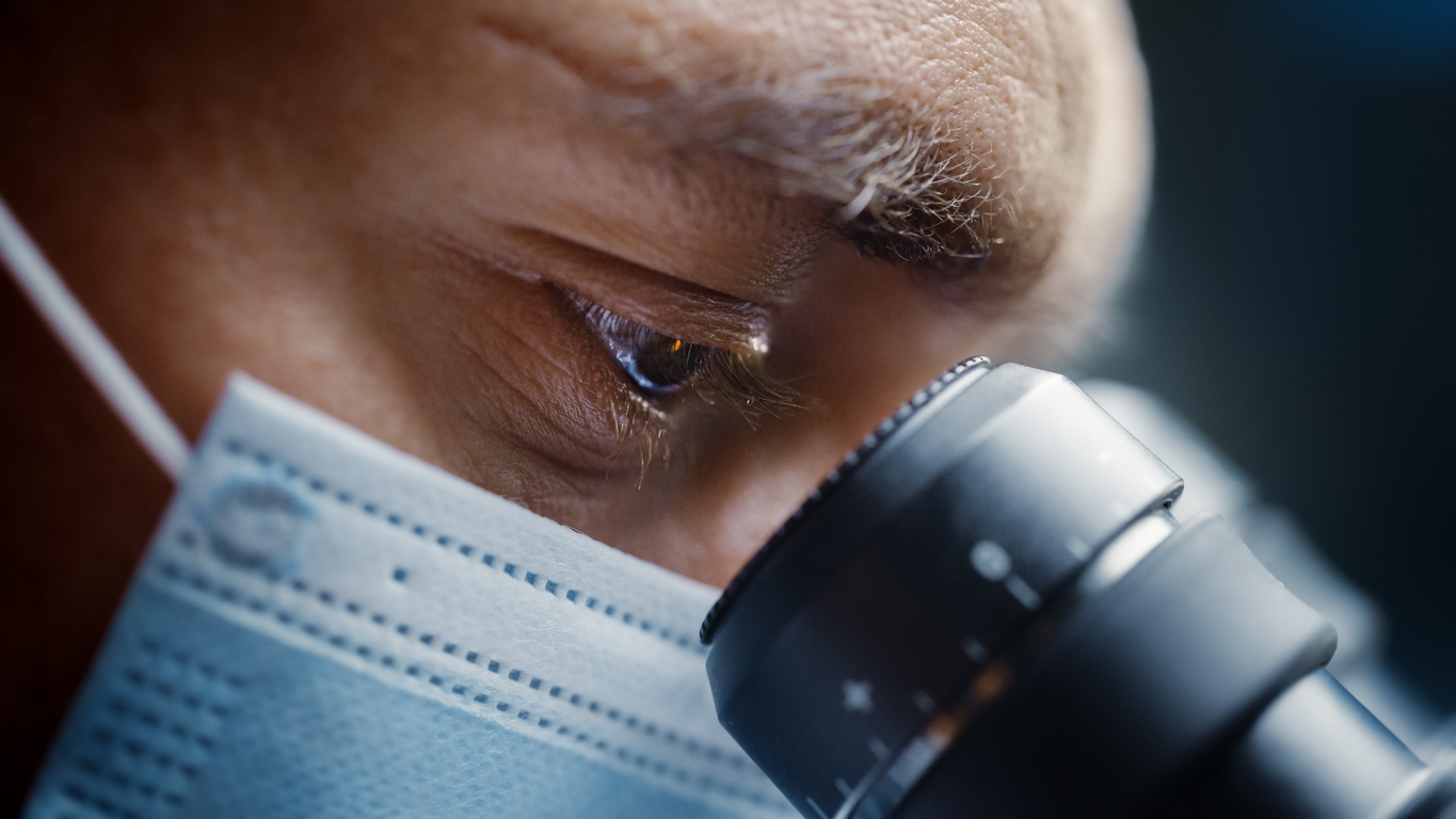 Scientist Wearing Surgical Mask and Looking into the Microscope