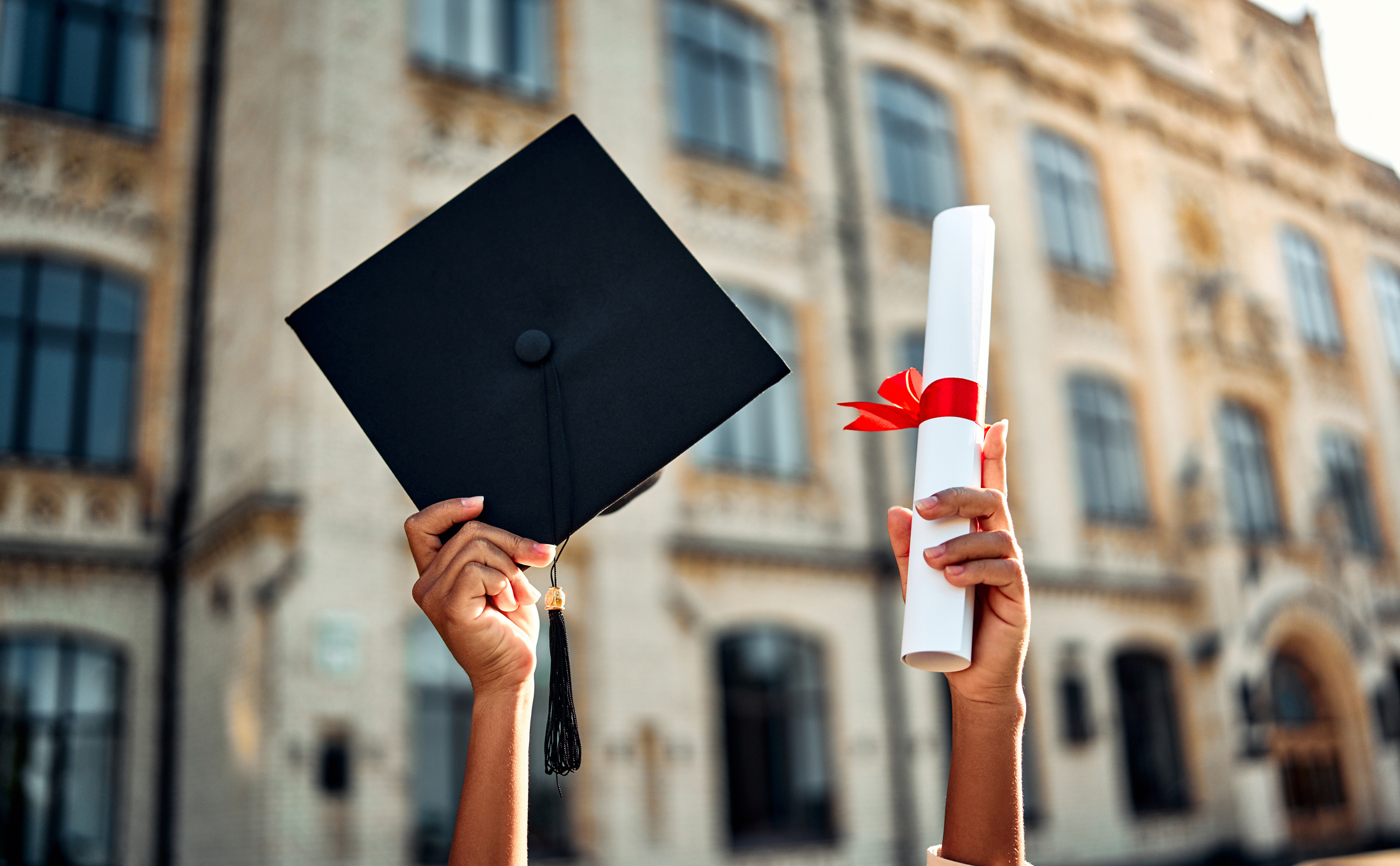 Cropped image of graduate holding academic hat and diploma with red ribbon. 