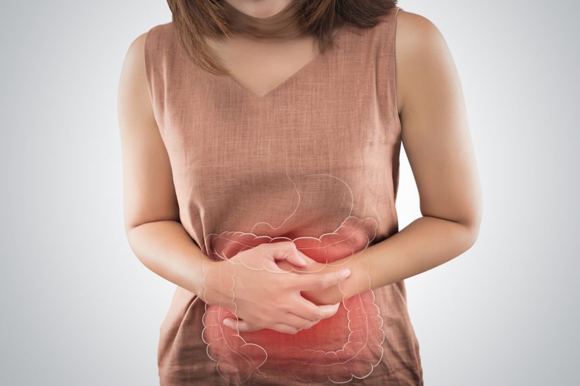 A woman holds her stomach, with outlined digestive tract.
