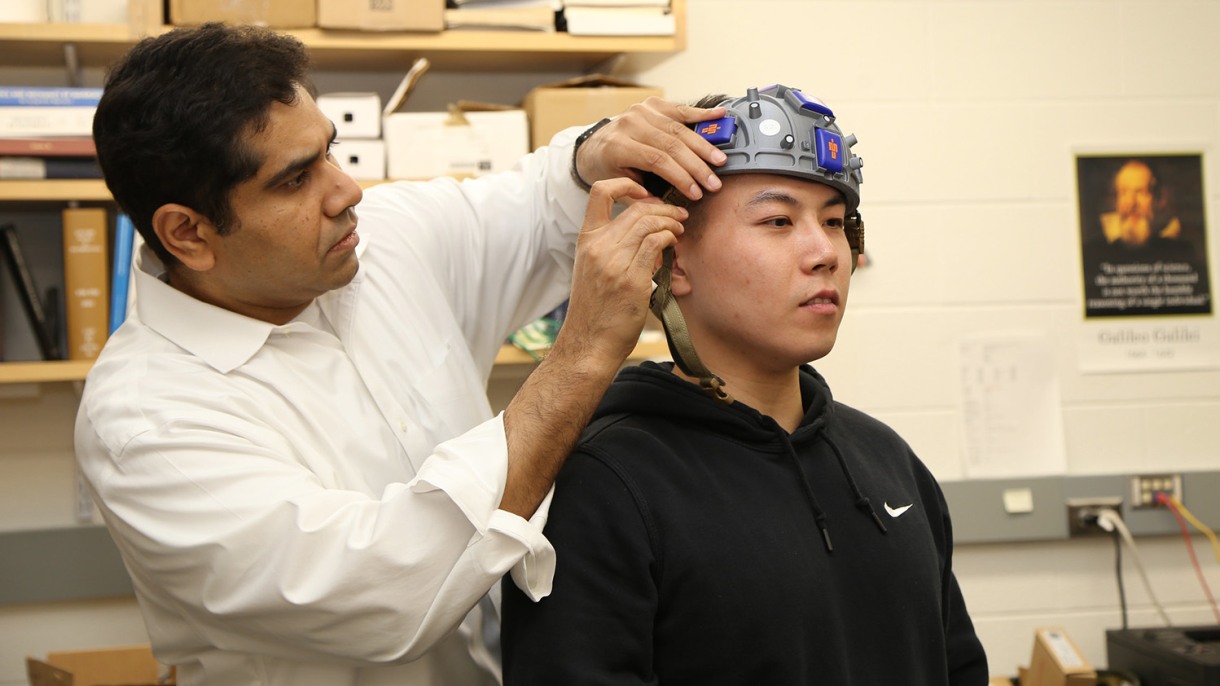 Haneesh Kesari (left) helps postdoctoral researcher Yang Wan to don the accelo-hat, which helps to measure forces in the brain associated with rapid head movements.
