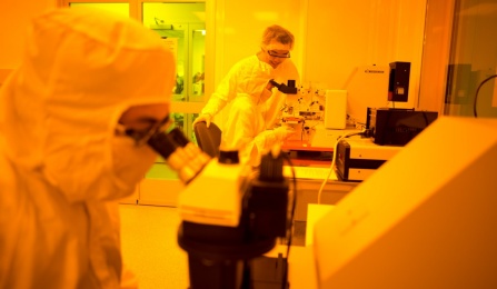 Two scientists in protective gear working with microscopes