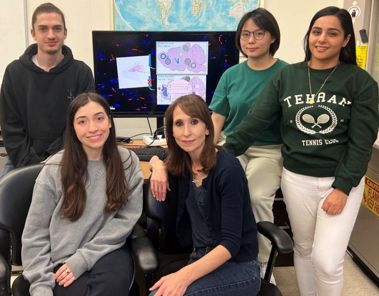 four students and one professor gathered for a picture in front of a computer screen showing a graphic from their work