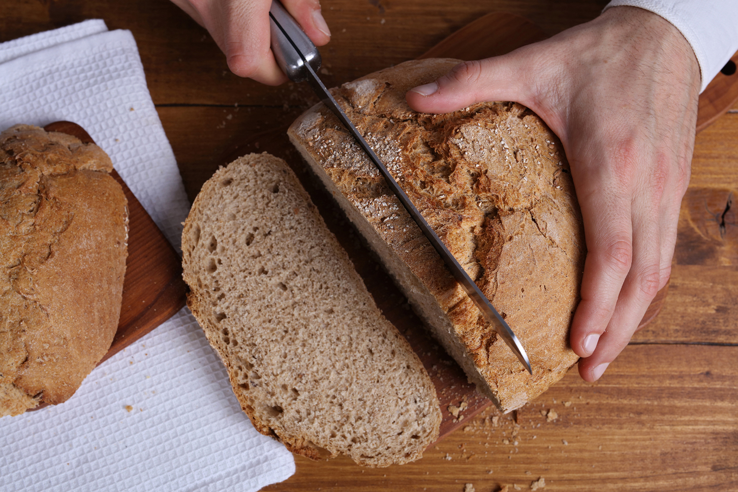 A loaf of bread getting sliced on a wooden cutting board